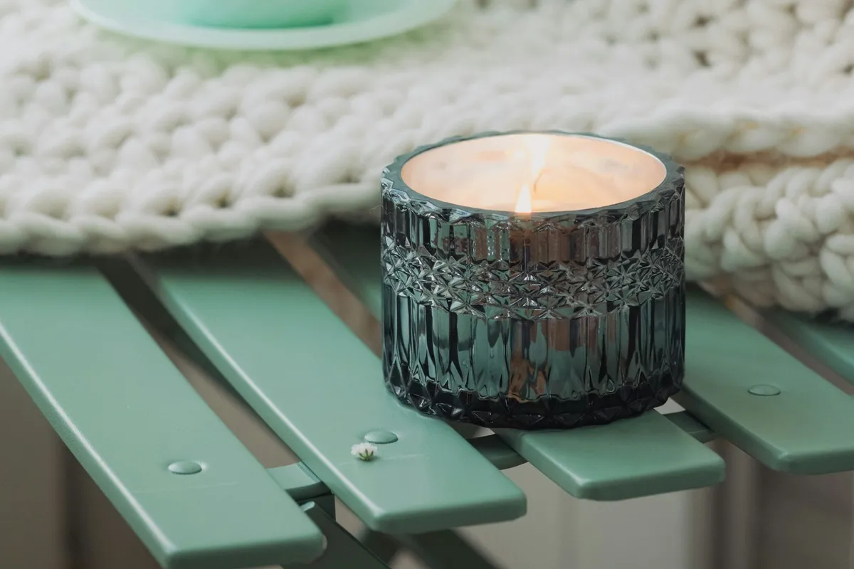 Steaming tea, a cream knit blanket and a lit candle on a sage-green table