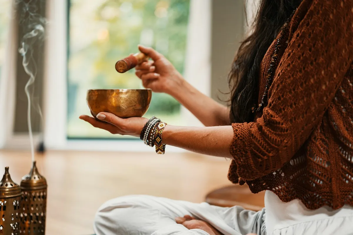 Woman in a knit sweater playing a singing bowl in a warmly lit room